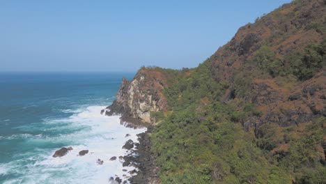 Aerial-view-of-rocky-cliff-coastline-with-ocean-waves-leading-up-to-it