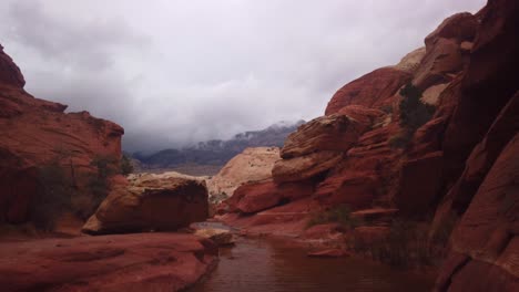 gimbal shot booming down from thick clouds to natural desert water tank in red rock canyon, nevada