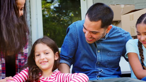 family sitting on steps of new home on moving in day