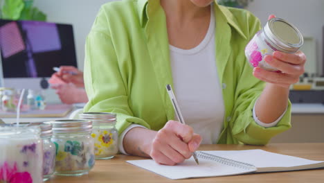 pareja dirigiendo un negocio en línea desde casa haciendo velas boutique escribiendo notas sobre productos