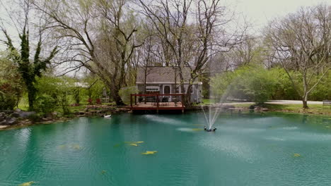 aerial view of private cottage with deck overlooking blue pond with fountain