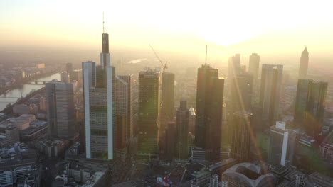 Beautiful-Sun-Rays-in-between-Skyscrapers-of-Frankfurt-am-Main,-Germany-Skyline-revealing-and-reflecting-in-windows,-Aerial-Establishing-Shot-slide-left