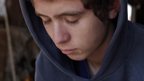 Closeup-of-the-face-of-a-young-teen-boy-sitting-in-a-garage-alone-looking-sad-and-depressed