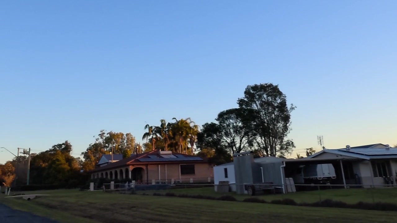 Luz dorada del atardecer ilumina una tranquila calle rural con casas y tendido eléctrico en Australia