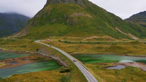 siguiendo un camión conduciendo a lo largo del puente fredvang en lofoten, norte de noruega, con hierba verde amarilla circundante y la montaña empinada en el fondo con pequeñas cabañas rojas en verano