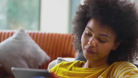 Primer-Plano-De-Una-Mujer-Relajándose-En-El-Sofá-De-Casa-Usando-Una-Tableta-Digital-Para-Transmitir-Películas