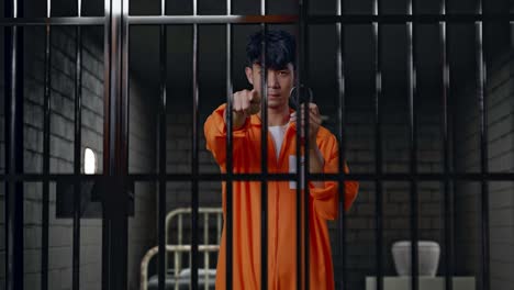 asian male prisoner standing in prison, showing the handcuffs and pointing his finger towards you