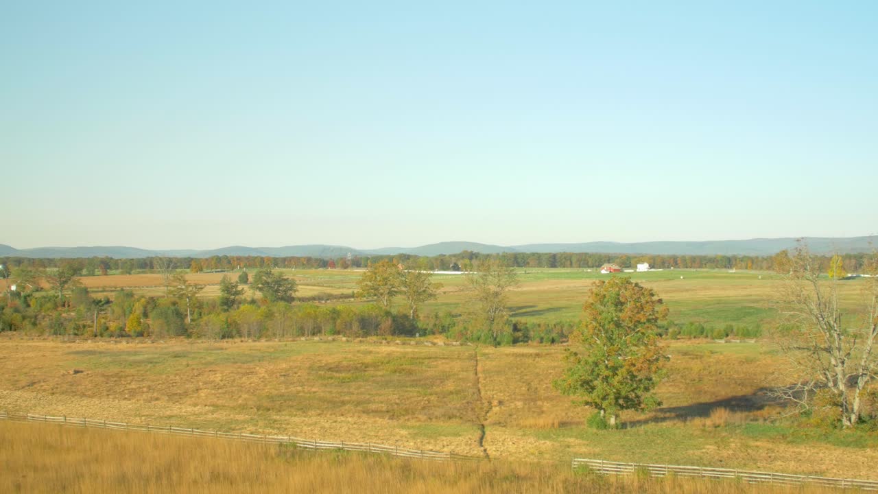 Beautiful scenic view of grasslands covered with yellow and green grass and a forest and cottages at a distance on a bright sunny day near the Civil War battlefields near Gettysburg, PA USA