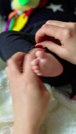 mother takes her baby's little feet in her arms. child lying on bed with a toy in his hands in blur. white backdrop. vertical video
