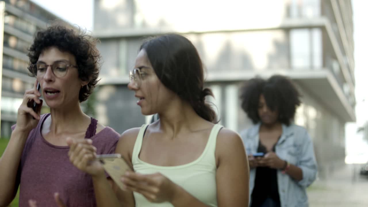 dos amigos sonrientes con dispositivos digitales caminando por la calle