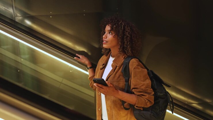 Giovane donna con lo zaino sulla scala mobile in una stazione moderna