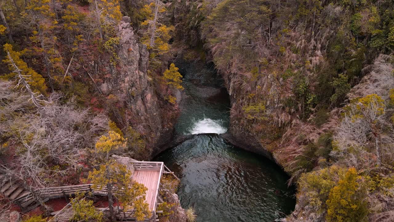 Forward drone aerial of emerald pool with viewing platform, Siete Tazas National Park, Ñuble, Chile through canyon with autumn forest surroundings