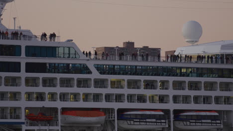 passengers standing along top deck of cruise ship during golden hour as it comes into dock in new york