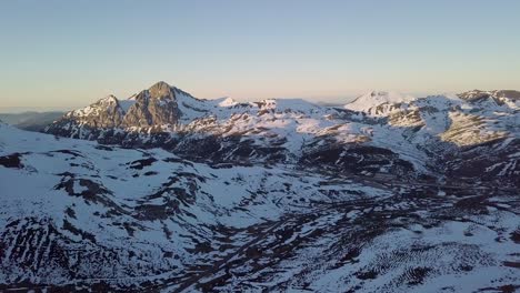 Aerial-View-Zooming-Out-of-Vast-Snowy-Mountainous-Landscape-During-Golden-Hour