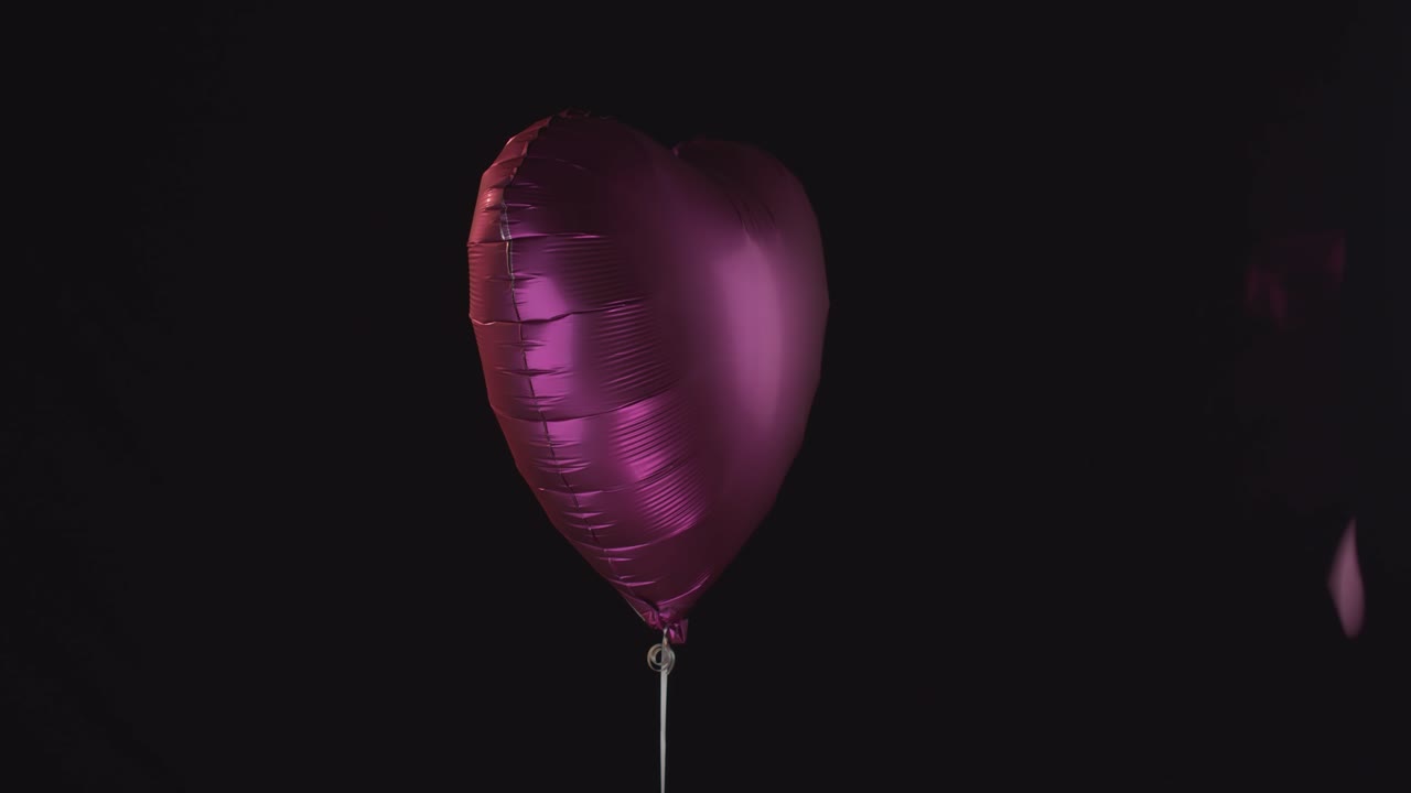Un palloncino a forma di cuore rosa brillante con cuori rosa che cadono tutt'intorno.