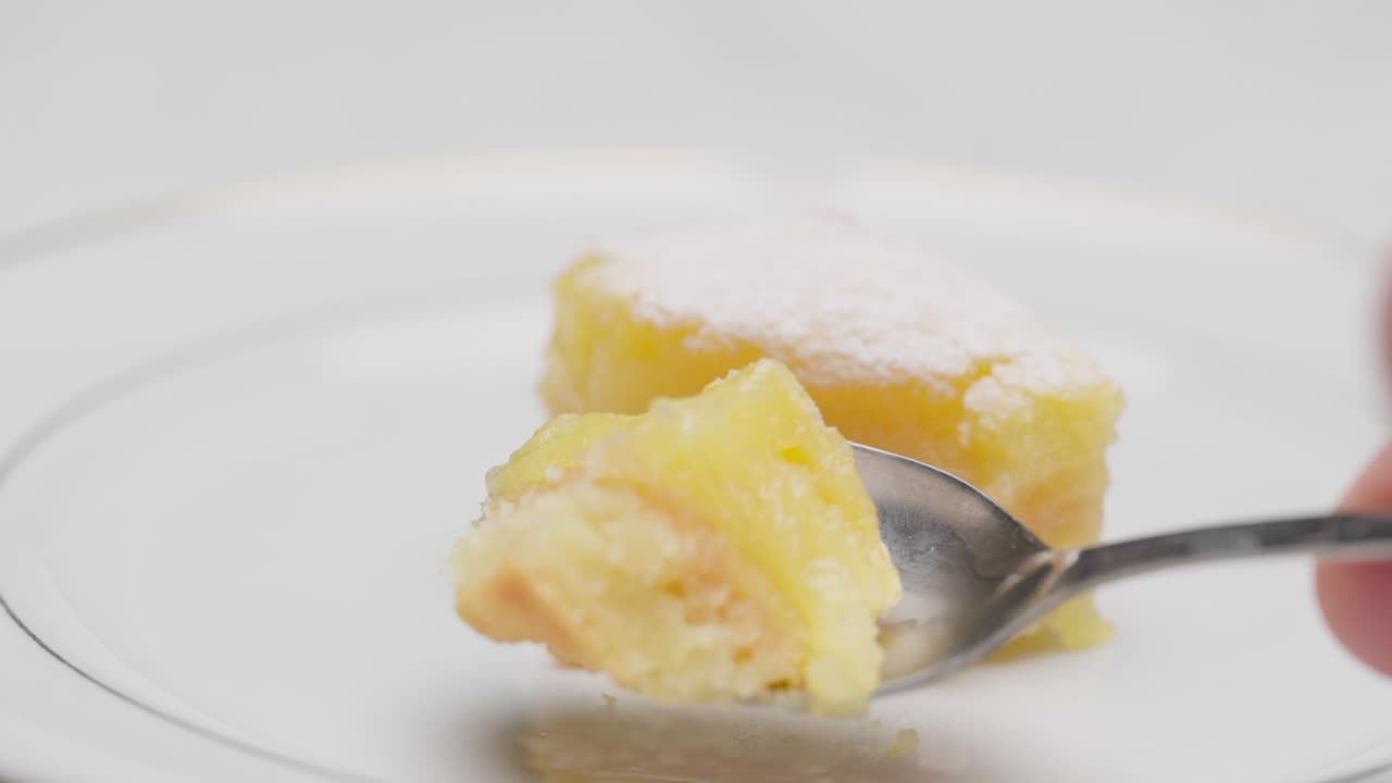 Primo piano di una fetta di torta al limone mentre un cucchiaio preme delicatamente la consistenza morbida e umida su un piatto bianco