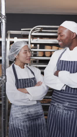 vertical video of portrait of happy diverse bakers talking with arms crossed in slow motion