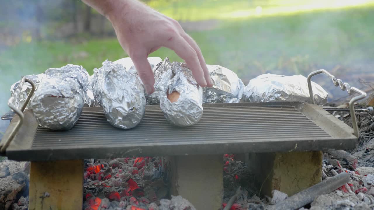야채를 요리하는 뒷마당 화재에서 석탄 위에 뜨거운 접시를 만지는 손의 클로즈업 샷