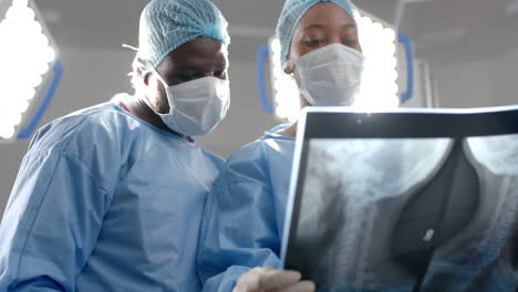 african american male and female surgeons looking at x-ray scans in operating theatre, slow motion