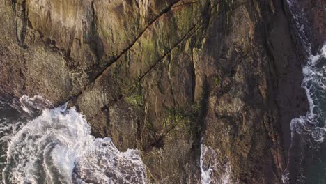 drone top view moving from near a rock at the shore where waves break to a far top view