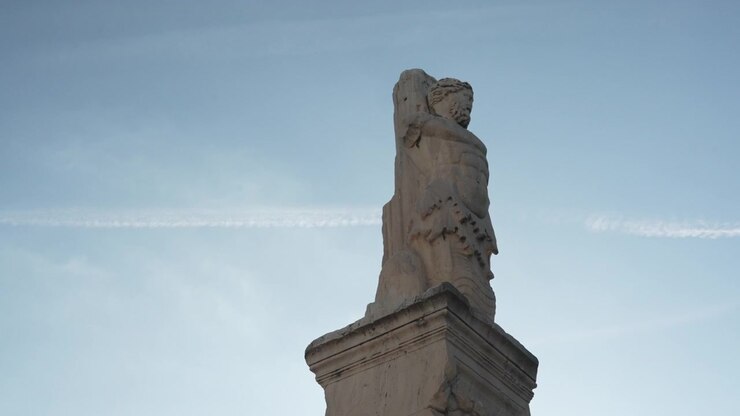 Statua in marmo di figura stoica romano-greca su sfondo di cielo blu.