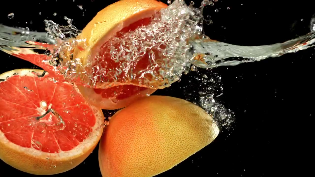 Mezzi pompelmi rossi freschi che schizzano nell'acqua al rallentatore