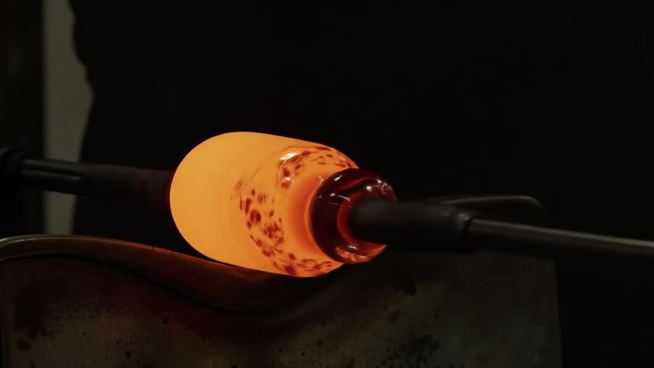 Skilled artisans create stunning glass pieces using molten glass in a workshop. The intricate process showcases the artistry and craftsmanship involved in glassblowing.
