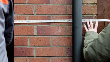 disparo de mano de una pareja midiendo el exterior de una casa con una cinta métrica