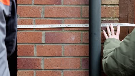 hand-held shot of a couple measuring the outside of a house with a tape measure