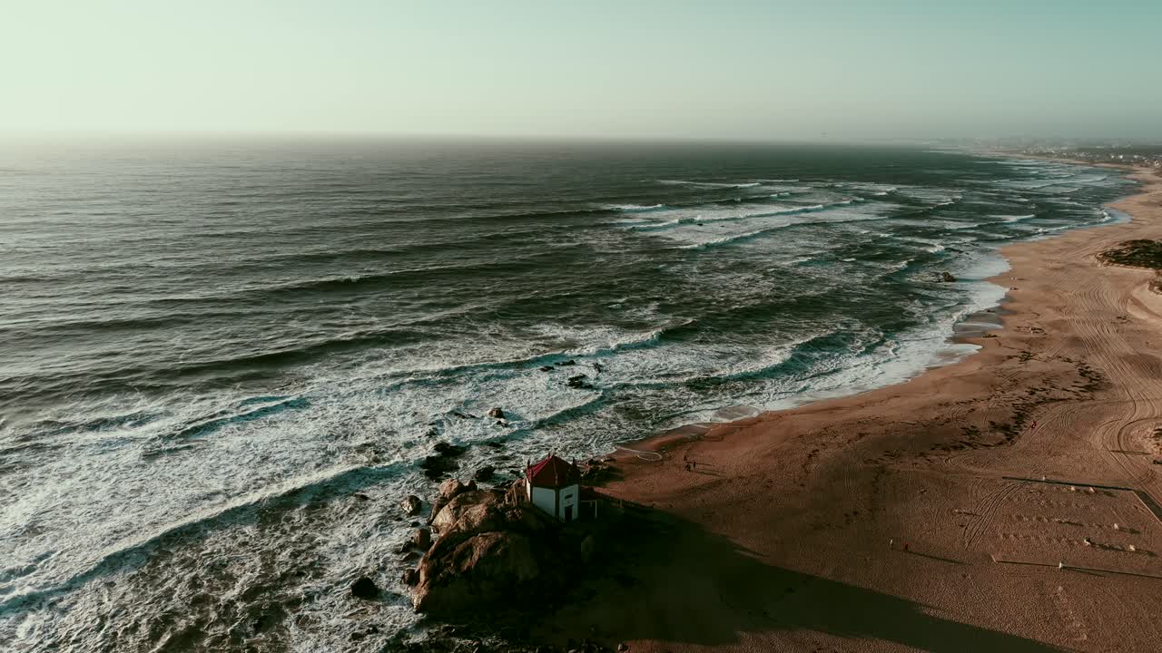 Aerial shot of Senhor da Pedra chapel on sandy beach by Atlantic Ocean in Gulpilhares Portugal