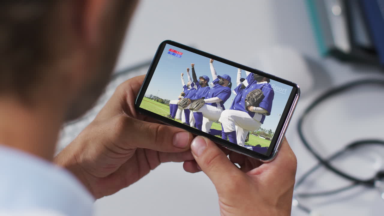 composición de un médico masculino viendo un juego de béisbol durante la covid 19 en un teléfono inteligente