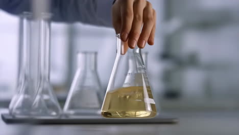 a hand holding an erlenmeyer flask with a yellowish liquid in a laboratory setting