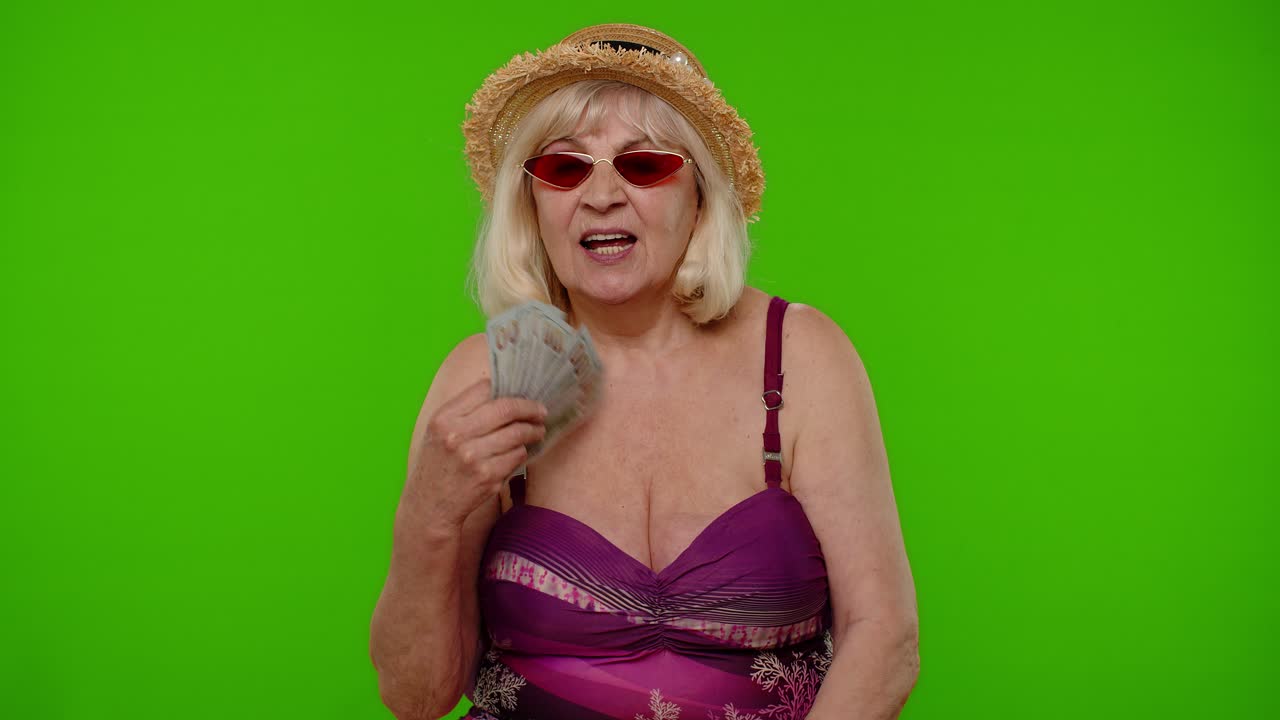 녹색 스크린에 돈을 들고 수영복을 입은 행복한 고위 여성