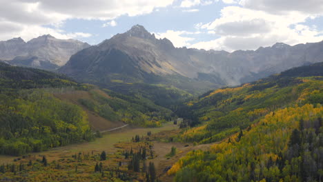 aerial shot forward of beautiful colorado mountains and bright yellow and orange aspen trees during autumn in the san juan mountains showing fall landscapes near mt