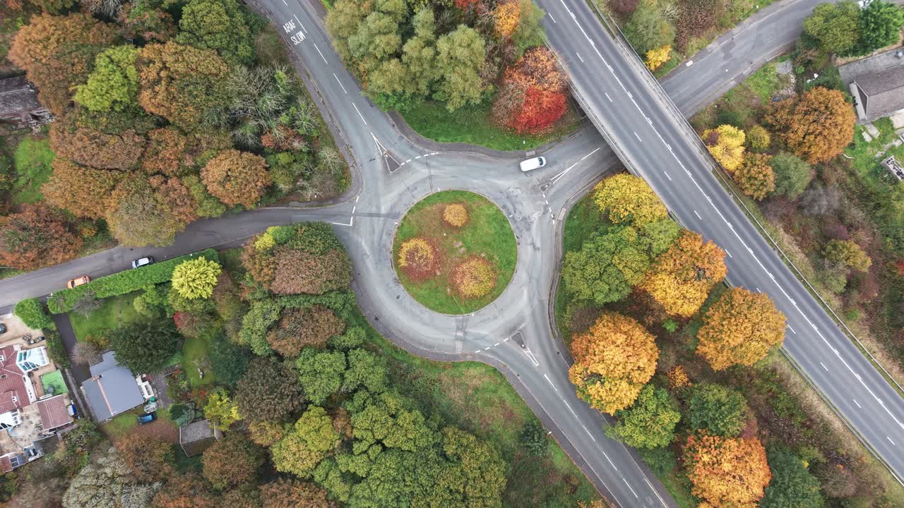 Rural roundabout with colourful autumn trees and passing traffic, aerial perspective