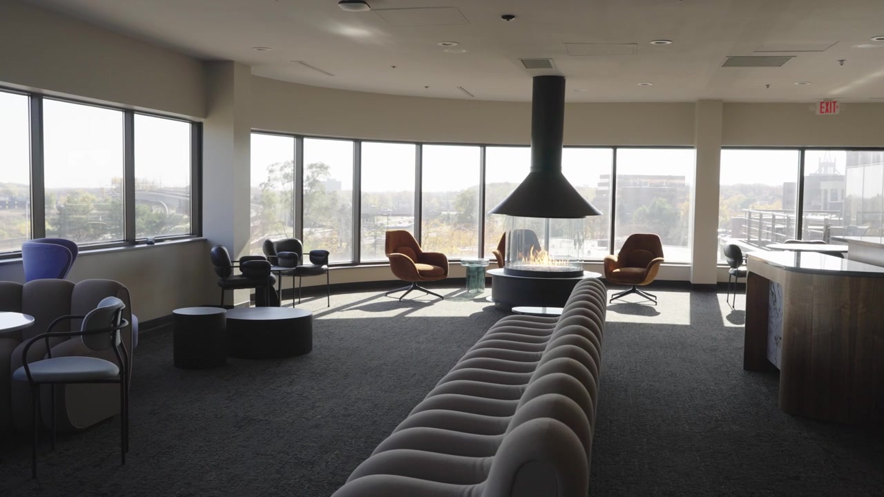 Elegant office lounge featuring a central fireplace, curved sofa, and natural light.