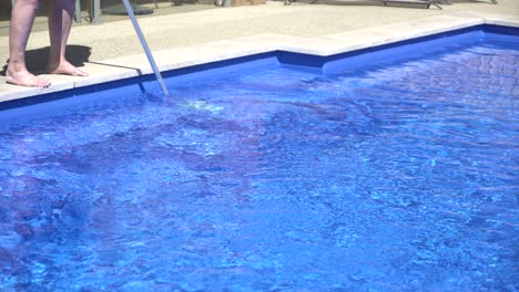 man cleaning blue pool sunny day