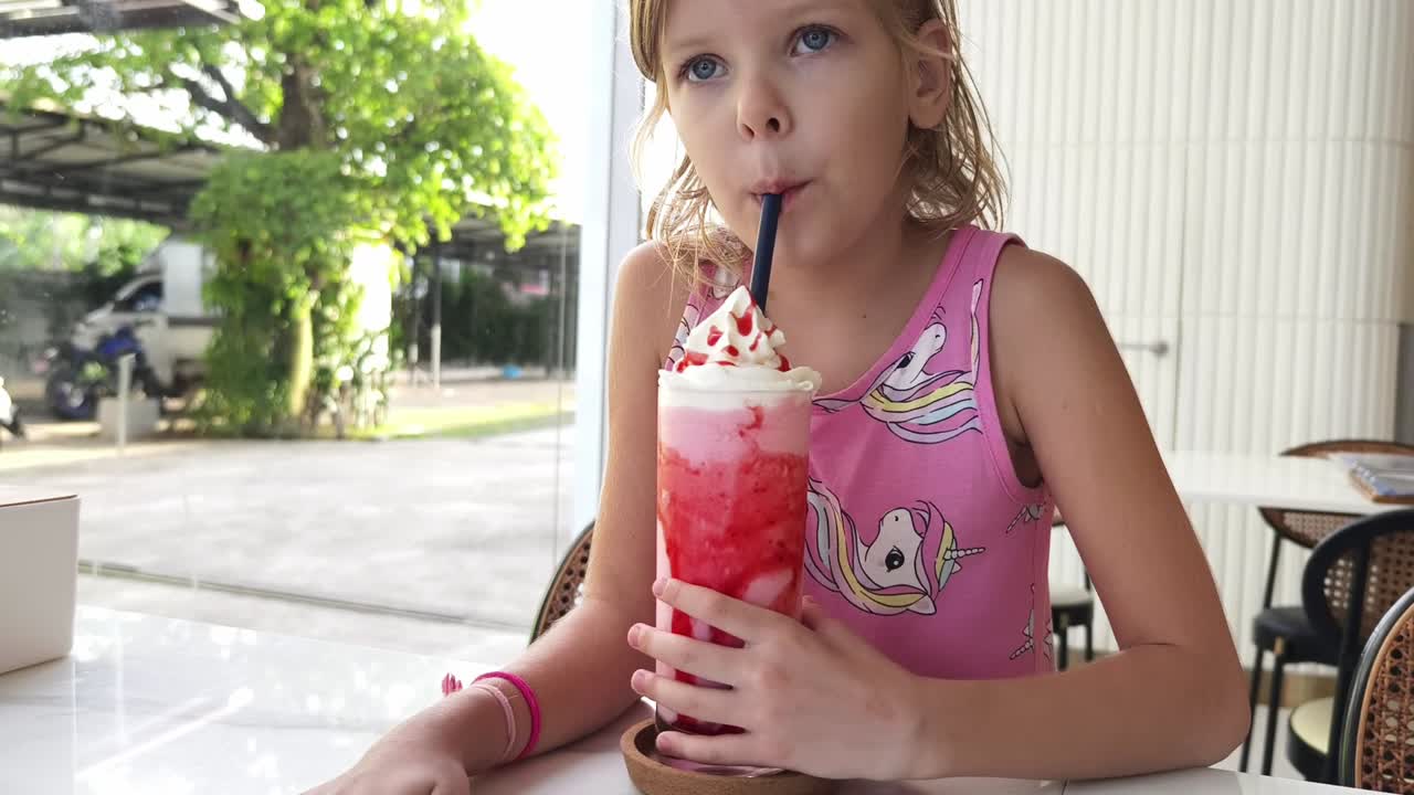Bambino che beve un frullato di fragole in un caffè