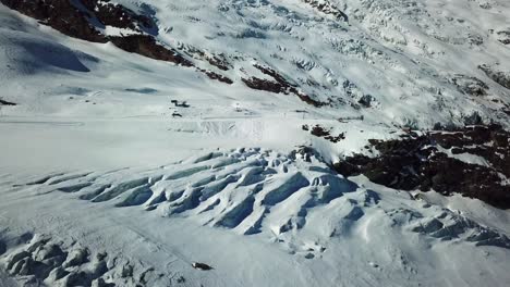 blue-glacier-with-crevices-in-the-swiss-alps,-ski-infrastructures-in-the-background