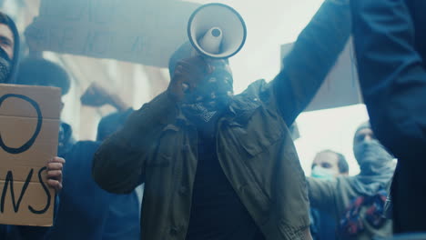 hombre afroamericano con bufanda en la cara y gritando con los brazos arriba en una protesta con un grupo multiétnico de personas en la calle