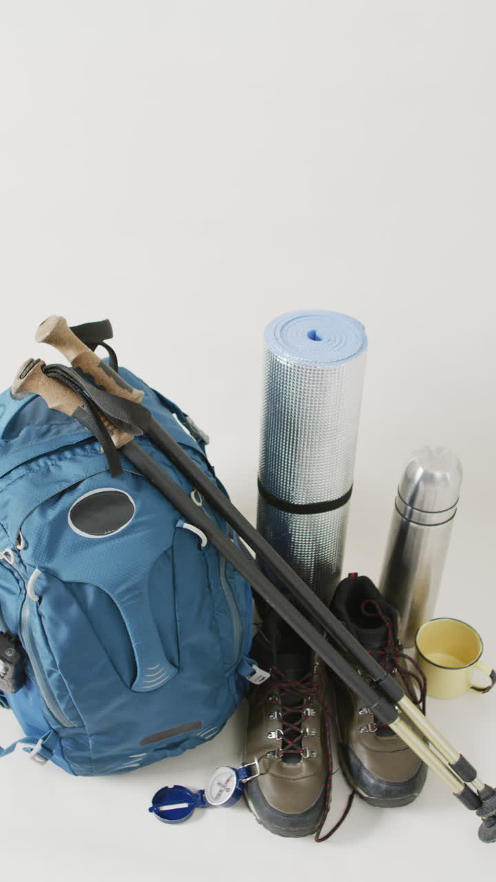 Vertical video of camping equipment with rucksack, poles, boots and copy space on white background