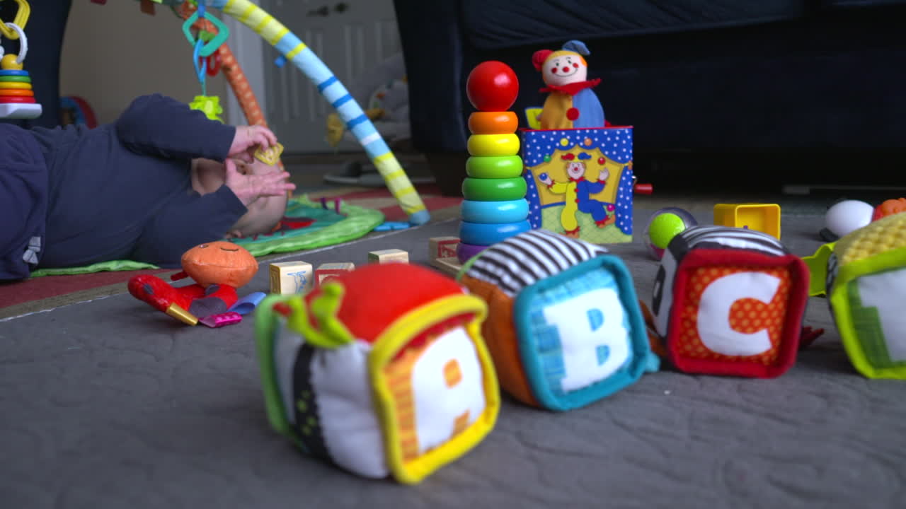 Bebê menino rolando no chão, brincando com brinquedos.