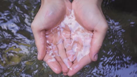 a hand grabs water from the stream. slow motion.