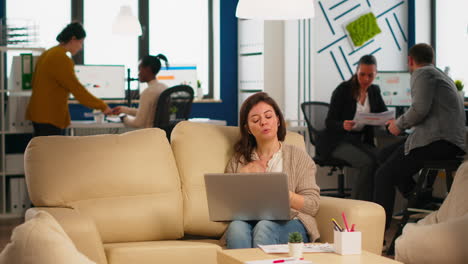 mujer gerente sentada en el sofá sosteniendo una computadora portátil y hablando en una llamada de video