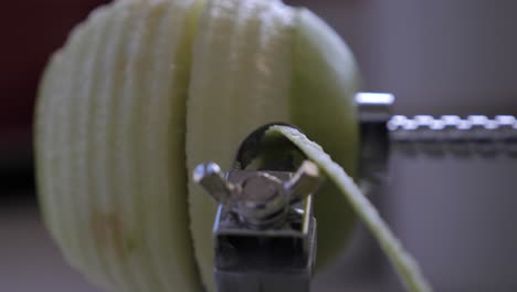 slow motion metal kitchen device peeling, cutting and core green juicy apple skin and flesh on kitchen bench with juice flying out