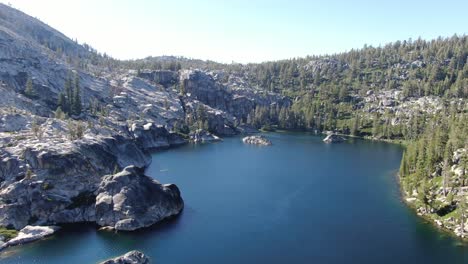 un dron de alta resolución de 4k rodó en círculo alrededor de un lago alpino de aguas cristalinas rodeado de árboles, rocas y acantilados en el desierto de california, perfecto para acampar, hacer caminatas y hacer mochileros al atardecer en verano.