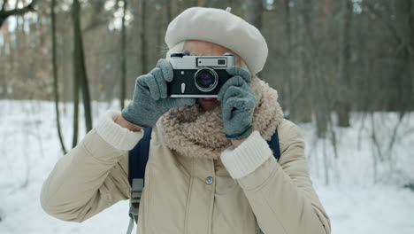 senior woman photographing in a snowy forest