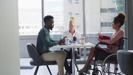 diverse business people discussing with disabled colleague and documents in creative office