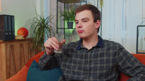 thirsty teen young man sitting at home holding glass of natural aqua make sips drinking still water