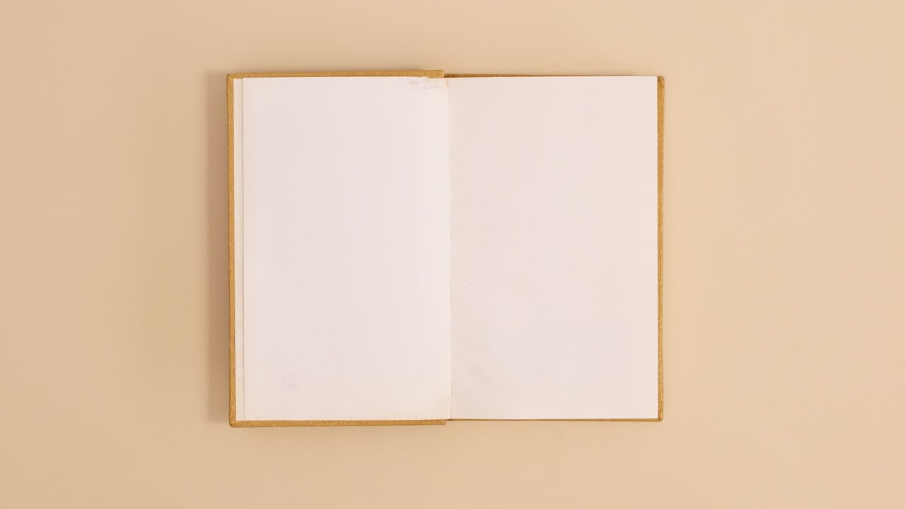 Golden hardcover vintage book appear and open with copy space on beige background. Stop motion flat lay